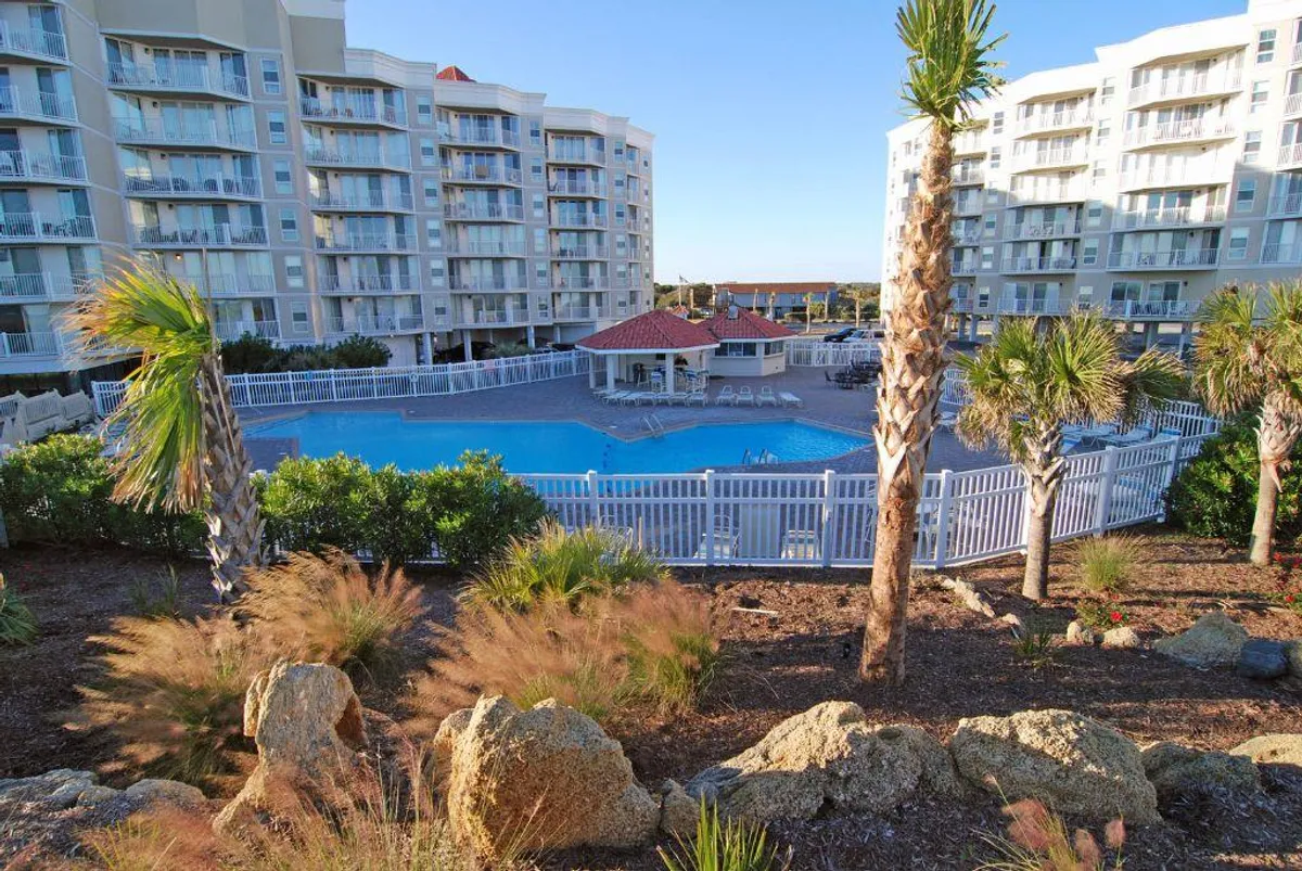 A sparkling outdoor swimming pool surrounded by palm trees and condominium buildings, with inviting lounge chairs and a tranquil atmosphere ideal for swimming and relaxation.