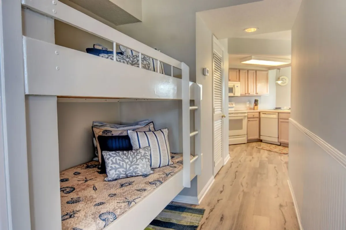 A cheerful interior shot with a hallway bunk bed, adorned with decorative pillows, and a partial view of the kitchen. The space feels cozy and playful, ideal for children or extra guests.