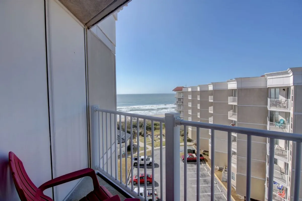 A stunning view from a private balcony, showcasing comfortable outdoor seating directly facing the ocean. The balcony overlooks sandy beaches, rolling waves, and the surrounding buildings, perfectly blending relaxation and scenic beauty.