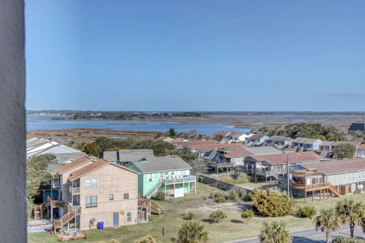 This view showcases colorful coastal homes set against marshland and distant water, evoking the broader neighborhood context. The tranquil scene suggests opportunities for nature walks, birdwatching, and photography, expanding the narrative beyond just the immediate resort.