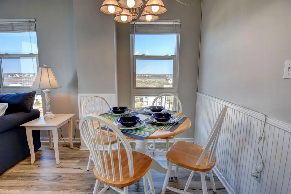 A welcoming dining area is shown with a large dining table set with plates, a statement chandelier above, window views, and a sofa nearby. The setting is ideal for family meals, special occasions, and enjoying views while dining.