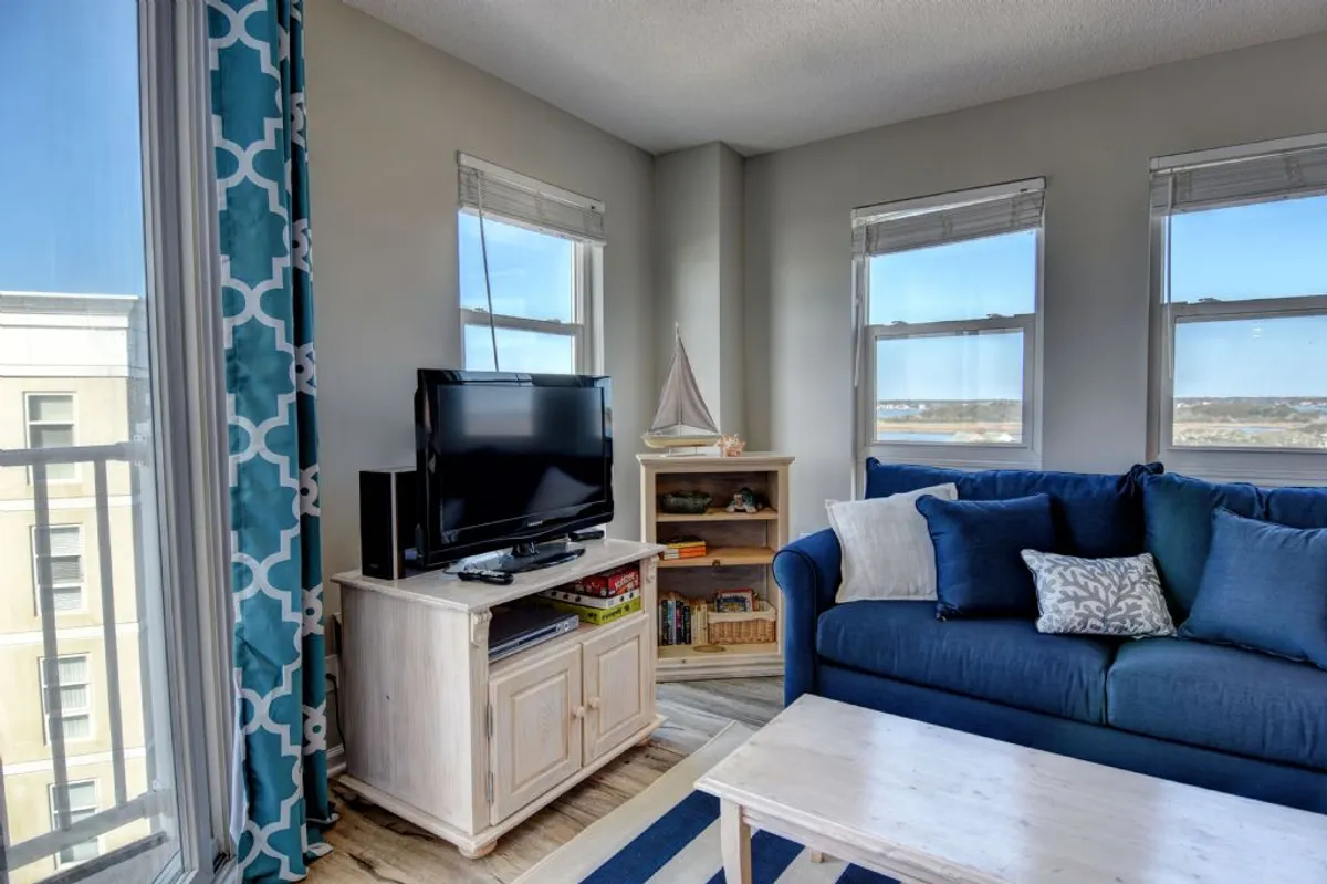 A comfortable living space featuring a sofa, television, bookshelf, and multiple windows that let in ample daylight. The area is arranged for both socializing and relaxation, with tasteful, homey decor and a warm, inviting mood.